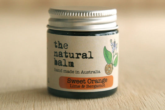 Jar of 'the natural balm' with a label indicating it's made in Australia and scented with sweet orange, lime, and bergamot.