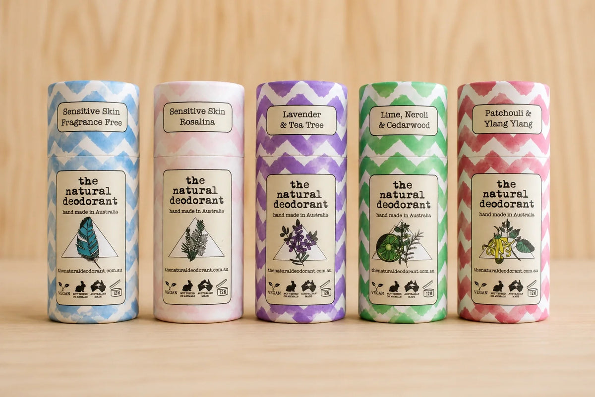 Set of five cylindrical The Natural Deodorant containers with colorful labels on a wooden surface.