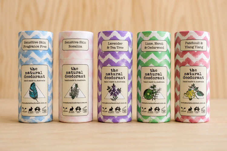 Set of five cylindrical The Natural Deodorant containers with colorful labels on a wooden surface.