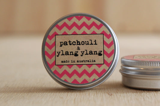 Tin with a chevron patterned lid labeled 'patchouli & ylang ylang made in australia' on a wooden surface.